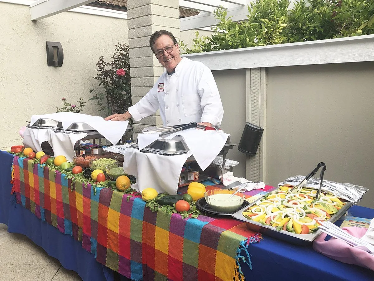 An Olamendi’s catering table with hot dishes, salad and colorful tablecloth